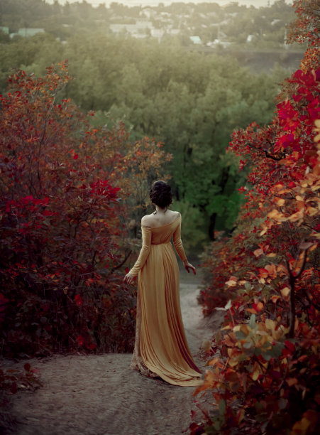 黄昏时分，穿着文艺复兴时期的黄色复古裙的公主在风景如画的秋山上散步。一张黑发女孩的照片，没有脸，只有背。艺术摄影。图片下载