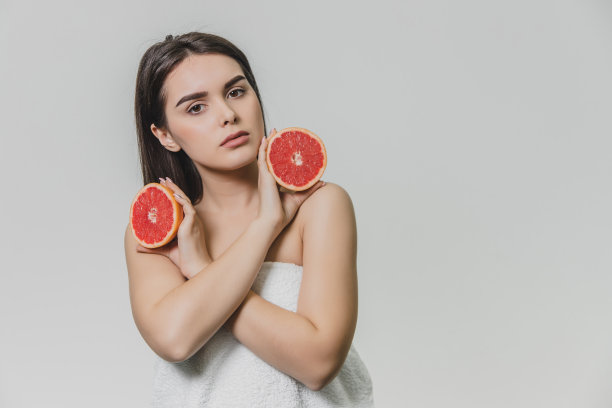 一个快乐的女孩用两半葡萄柚围在脸上。她微笑着，期待着幸福。孤立在背景中图片下载