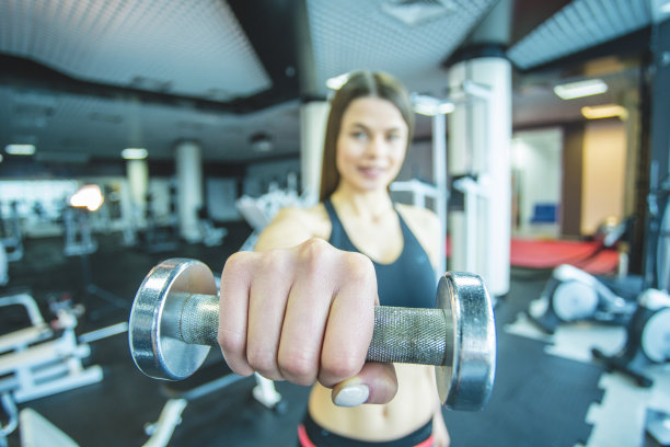 运动的女人在体育馆里举着哑铃。特写图片下载