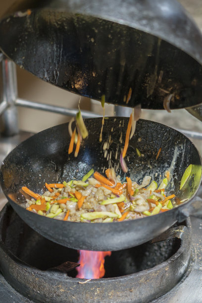 专业厨师和消防。在篝火上烹饪蔬菜和食物。专业厨师烹饪火焰风格。他用明火在平底锅里做菜。垂直的照片。图片下载