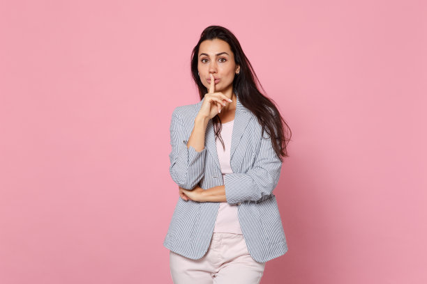 漂亮的年轻女子在条纹夹克说嘘，安静的手指在嘴唇嘘手势孤立在粉色柔和的背景在工作室。人真诚情感，生活理念。模拟拷贝空间。图片下载