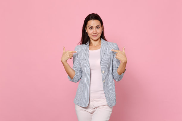 肖像微笑美丽的年轻女子在条纹夹克指着食指在自己孤立在粉红色的粉彩墙背景。人真诚情感，生活理念。模拟拷贝空间。图片下载