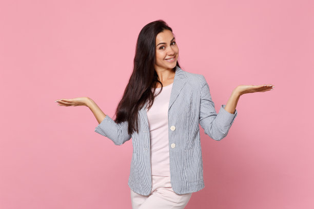 微笑的年轻女子的肖像在条纹夹克展开和指向一边孤立的粉色粉彩墙背景在工作室。人真诚情感，生活理念。模拟拷贝空间。图片下载