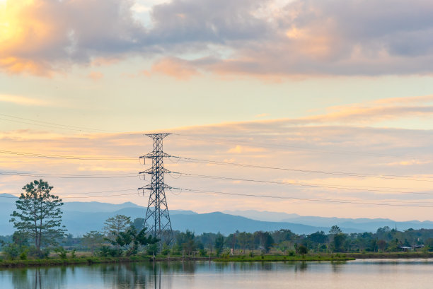 高电压电力站背景是色彩斑斓的日落天空与山和湖。图片下载