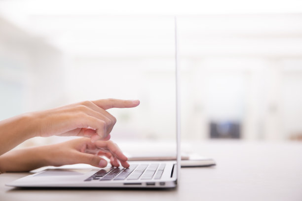 特写年轻女性的手使用笔记本电脑，并指向屏幕在现代办公室或阁楼附近的窗户。图片下载