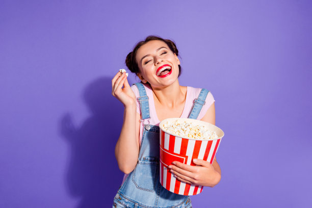 近距离的照片美丽惊人的她她的夫人两个包子看最喜欢的喜剧演员电视节目拿爆米花桶穿休闲t恤牛仔裤牛仔工作服衣服孤立的紫色紫罗兰的背景图片下载