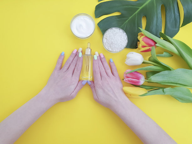 女性的手指甲，化妆品霜，怪物郁金香叶上的彩色背景图片下载