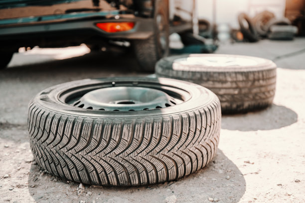 旧轮胎在汽车修理厂地面上的照片。在后台的车。图片下载