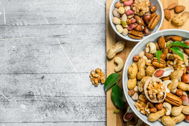 不同类型的坚果在碗和绿叶。图片下载