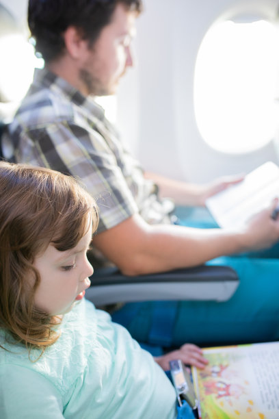 可爱的小女孩和她的父亲一起乘飞机旅行，坐在飞机窗边看书图片下载