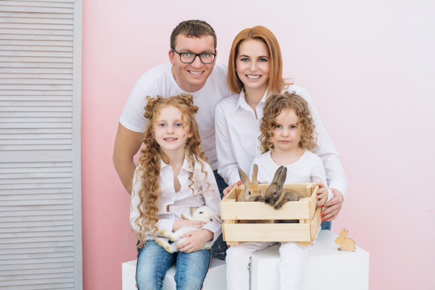 幸福的家庭妈妈，爸爸，两个女儿和毛茸茸的动物兔子在粉红色的背景美丽的微笑图片下载