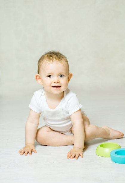 快乐的婴儿穿着白色紧身衣坐在一个轻便的地板上图片下载