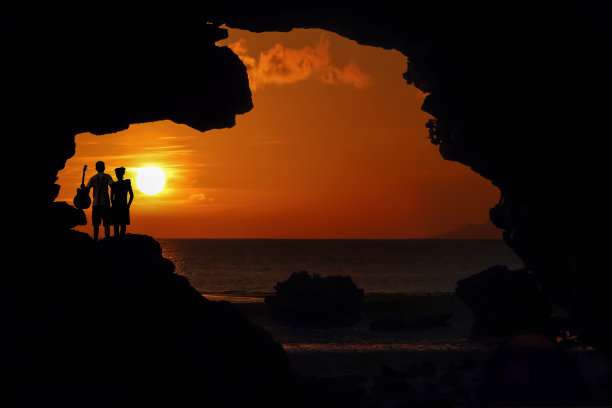 一对情侣站在海边的岩石上，红天日落。图片下载