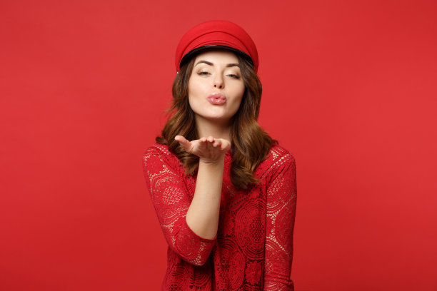 美丽迷人的年轻女子的肖像在蕾丝连衣裙，帽子吹送飞吻孤立在明亮的红色墙壁背景在工作室。人真诚情感，生活理念。模拟拷贝空间。图片下载