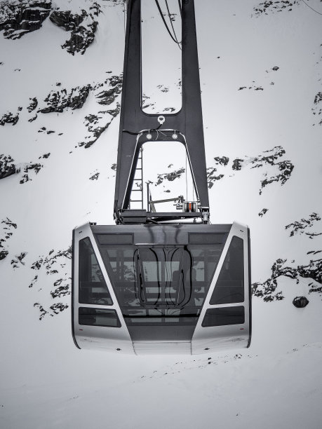 黑白近景的现代玻璃滑雪缆车缆车与白雪覆盖的山为背景图片下载
