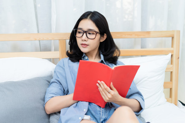 年轻的亚洲妇女在家里的床上看书。生活方式和放松的概念。图片下载