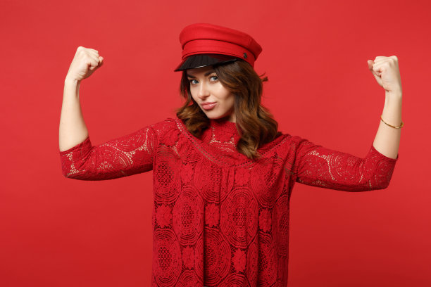 迷人的强壮的年轻女子的肖像在蕾丝连衣裙和帽子显示二头肌隔离在工作室明亮的红色墙壁背景。人真诚情感，生活理念。模拟拷贝空间。图片下载