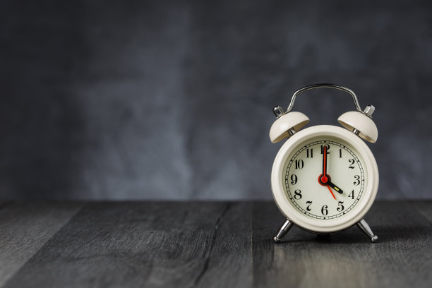 钟表指针在4点钟，闹钟在5点钟。复古/复古的白色模拟闹钟放在木桌上，黑色背景上有拷贝空间图片下载