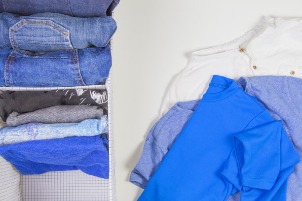 垂直存放衣物，整理房间，打扫房间的概念。把叠好的衣服放在篮子里，白色背景上放一堆没拿的衣服图片下载
