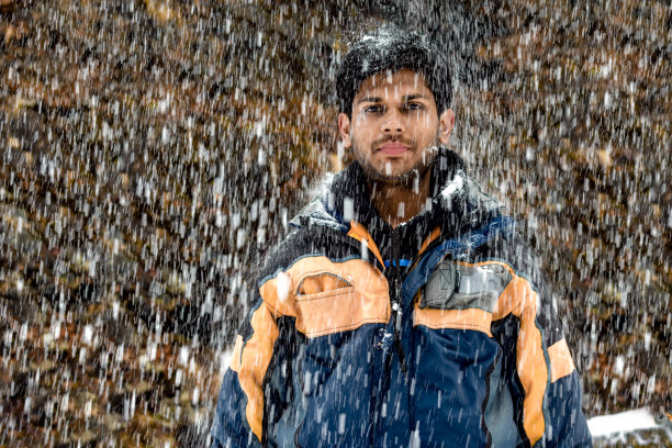20岁出头的英俊印度年轻男子身穿滑雪服，在圣诞节前夕的冬季大雪中静止站立并摆姿势图片下载