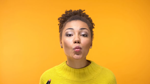 黑人女子手握口红，在镜头前飞吻，妆容自然图片下载