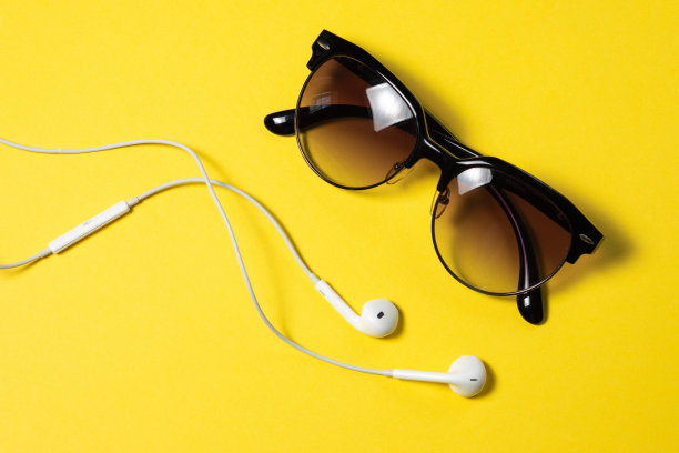 黑屏智能手机通过黄色背景顶视图的螺旋线连接耳机，太阳镜图片下载