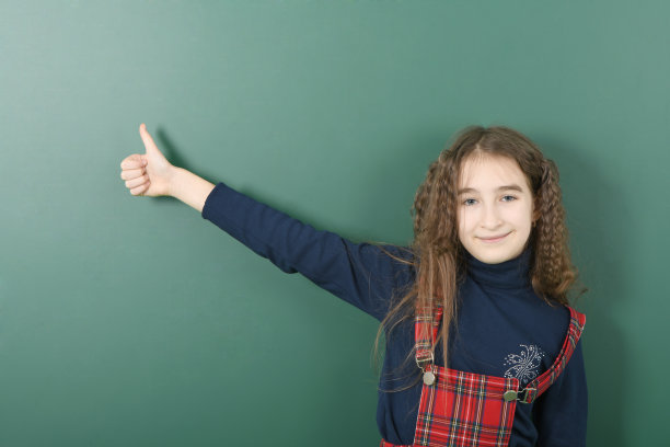 女学生在绿色学校董事会附近。顽皮的小女孩翘起了手指。图片下载