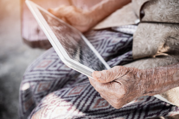 快乐的亚洲老妇人/祖母微笑着使用平板电脑手指在触摸屏上打字聊天短信给孙辈图片下载