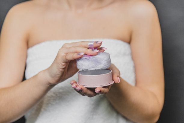 近距离肖像的年轻女孩身体与粉色粉扑。她穿着白毛巾。女孩双手捧着粉扑。照片没有脸。图片下载