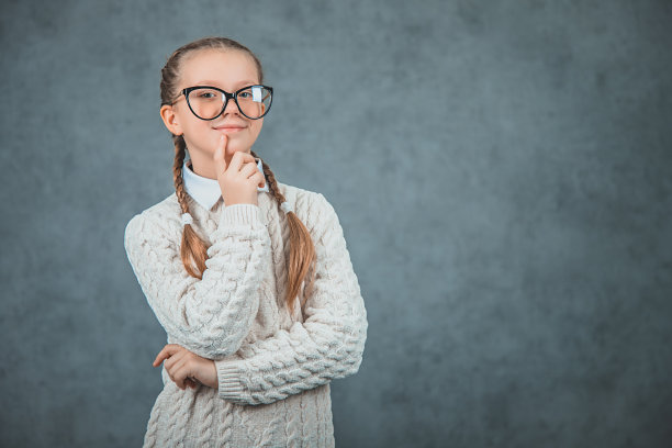 年轻的金发学生女孩穿着好看和舒适的毛衣和眼镜是孤立的灰色背景。她看起来很自信，面带微笑，双臂交叉，手放在下巴上。图片下载