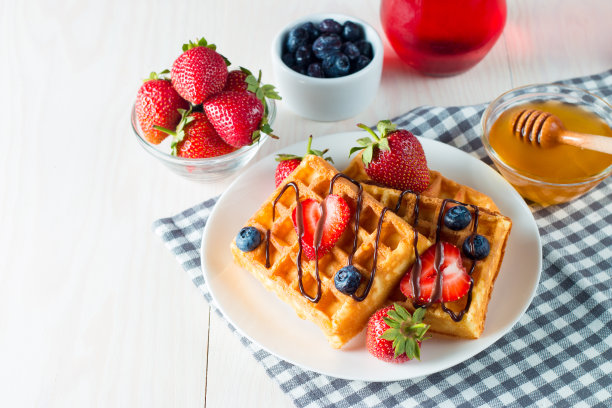 新鲜的自制食物的照片，浆果比利时华夫饼与蜂蜜，巧克力，草莓，蓝莓，枫糖浆和奶油。健康的早餐甜点搭配果汁。图片下载