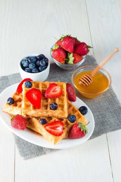 新鲜的自制食物的照片，浆果比利时华夫饼与蜂蜜，巧克力，草莓，蓝莓，枫糖浆和奶油。健康的早餐甜点搭配果汁。图片下载