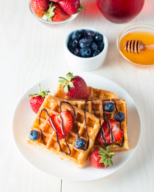 新鲜的自制食物的照片，浆果比利时华夫饼与蜂蜜，巧克力，草莓，蓝莓，枫糖浆和奶油。健康的早餐甜点搭配果汁。图片下载