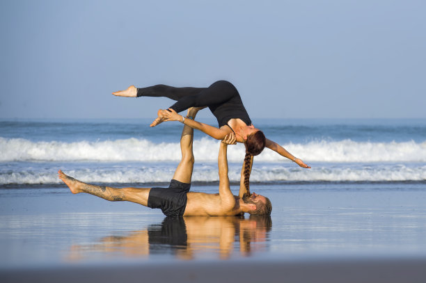 年轻迷人和美丽的杂技演员夫妇练习杂技瑜伽集中保持平衡练习瑜伽在海滩上放松和冥想的概念和健康的生活方式图片下载