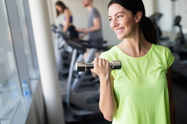 年轻漂亮的女人在健身房用哑铃锻炼身体图片下载