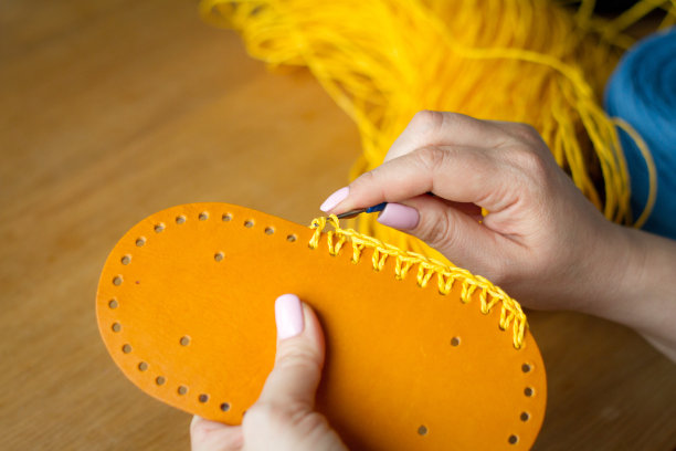 一个年轻女子的手用黄色的纱线在一个轻木制的表面上编织钩针。换一袋新的纱线。图片下载