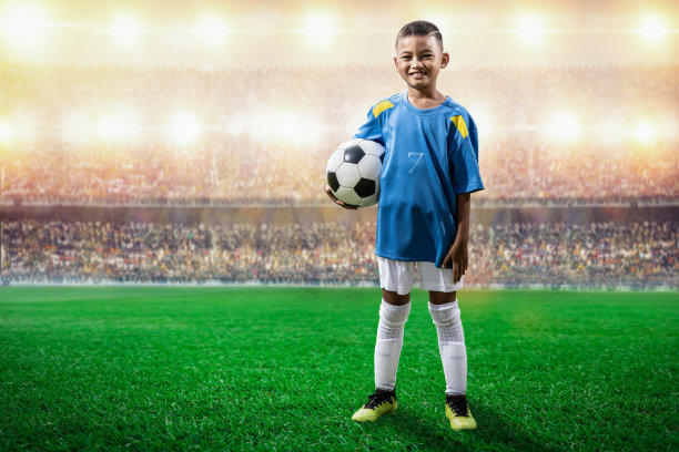 身穿蓝色球衣的亚洲足球孩子球员站在体育场的镜头前摆姿势图片下载
