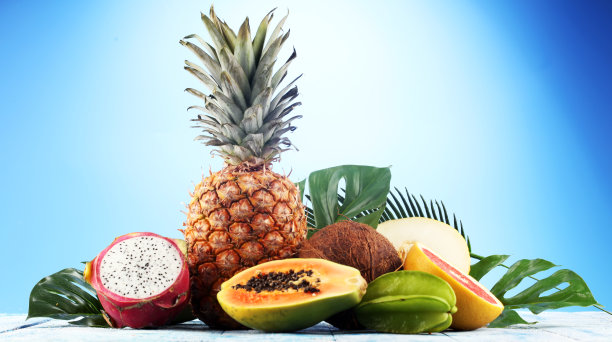 新鲜的热带水果在海滩上与棕榈叶。各种热带水果，橙子，香蕉或菠萝和芒果图片下载