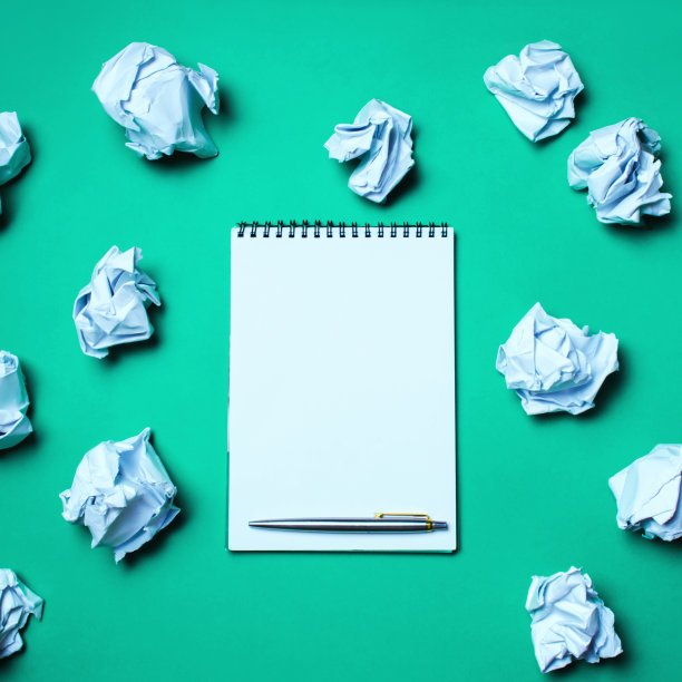 白色笔记本和钢笔在绿色背景的纸球。产生想法，创造新想法的概念。纸球到处都是。搜索的决定。坏主意。业务图片下载