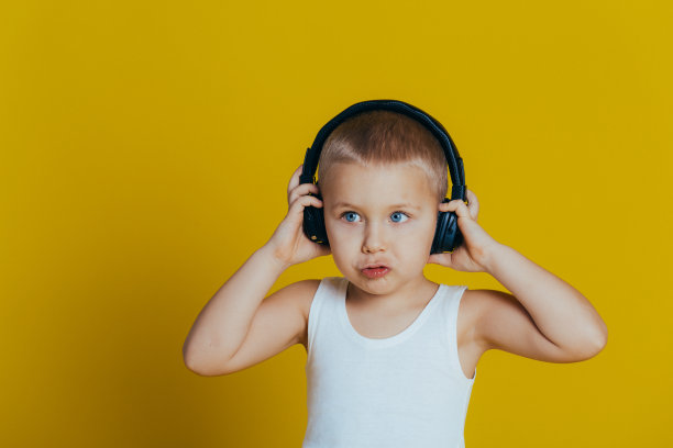 一个迷人的微笑男孩的肖像，穿着白色t恤听音乐通过耳机的特写，在黄色的背景图片下载