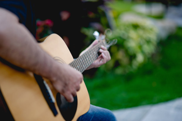 一个吉他手的图片，一个年轻人坐在一个自然的花园里弹吉他，音乐的概念图片下载