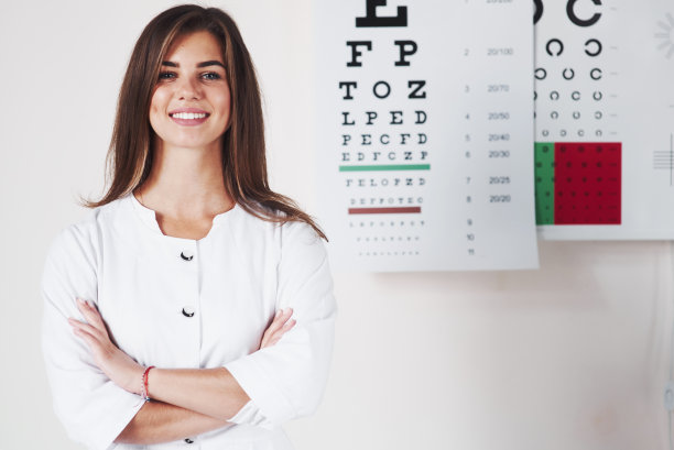 双手交叉。美丽的女眼科医生的照片站在黑板的背景与字母图片下载