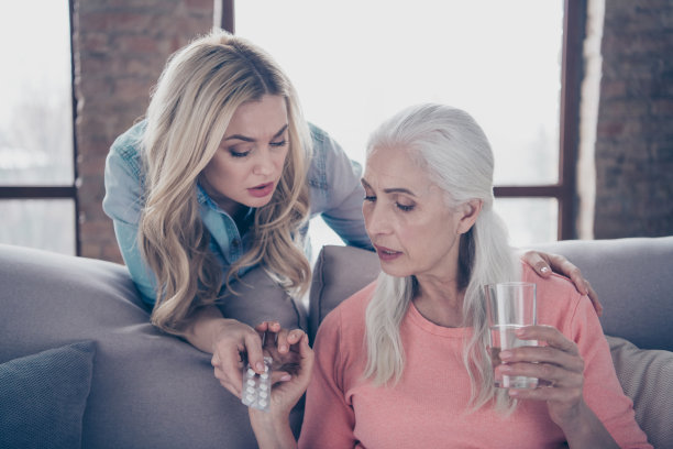 近距离的照片两人，她，她的女士，孙女担心带药，改善健康状况，奶奶，抱，拿，手，手臂，玻璃药丸，偏头痛，头痛，头痛，坐沙发，沙发，沙发，房子，室内图片下载
