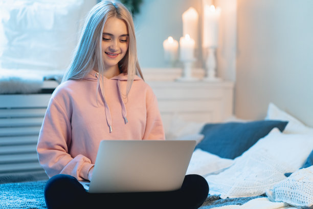 年轻女子坐在家里的床上使用笔记本电脑的特写图片下载