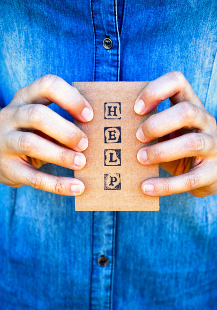 女人手里拿着写着“帮助”的黑色字母邮票纸板。图片下载