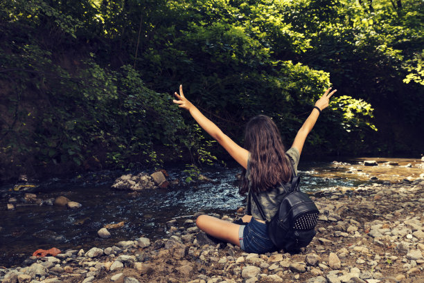 一个背着黑色帆布背包的年轻女孩坐在城市公园的河岸上图片下载