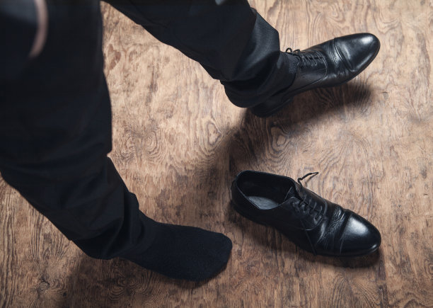 穿着黑色皮鞋的人脚踩在木地板上。图片下载