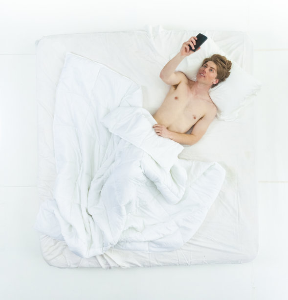 英俊的男人躺在床上，赤膊上阵，还在打电话图片下载