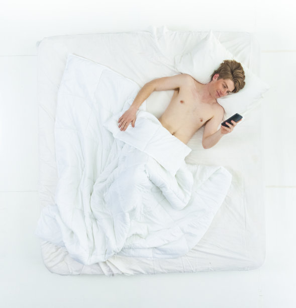 英俊的男人躺在床上，赤膊上阵，还在打电话图片下载