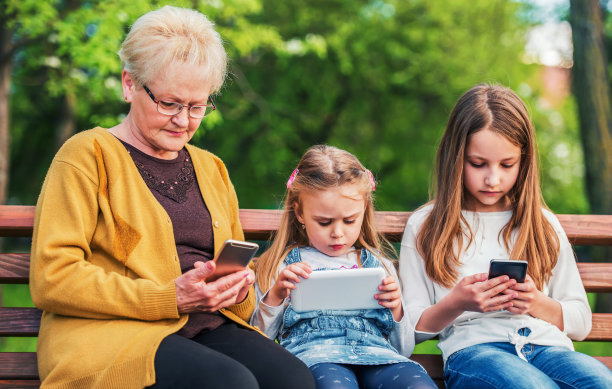家人疏远。奶奶坐在公园里玩智能手机，而她的孙女们玩手机和平板电脑。家庭、生活方式、科技理念图片下载
